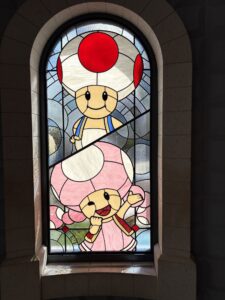 Arched window with two mushroom-headed characters in leaded stained glass