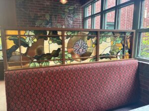 Stained glass booth divider with oak leaves and a compass medallion from a different angle