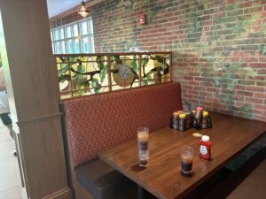 Booth divider in stained glass beside a wooden table with a window beyond