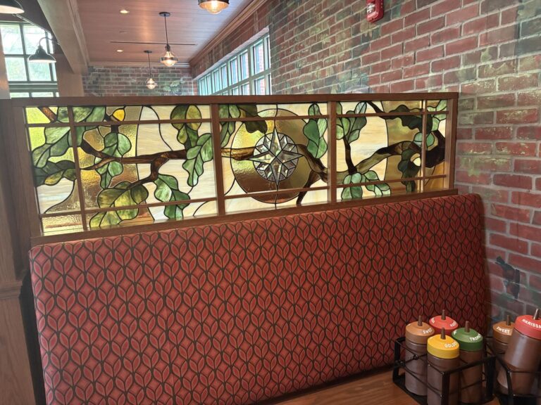 Stained glass divider above a red booth seat showing oak branches and a compass design