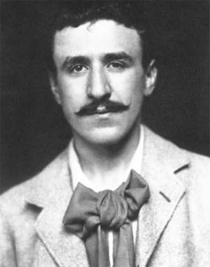 Black and white portrait of Charles Rennie Mackintosh as a young man, with a moustache and a large loose bow tie