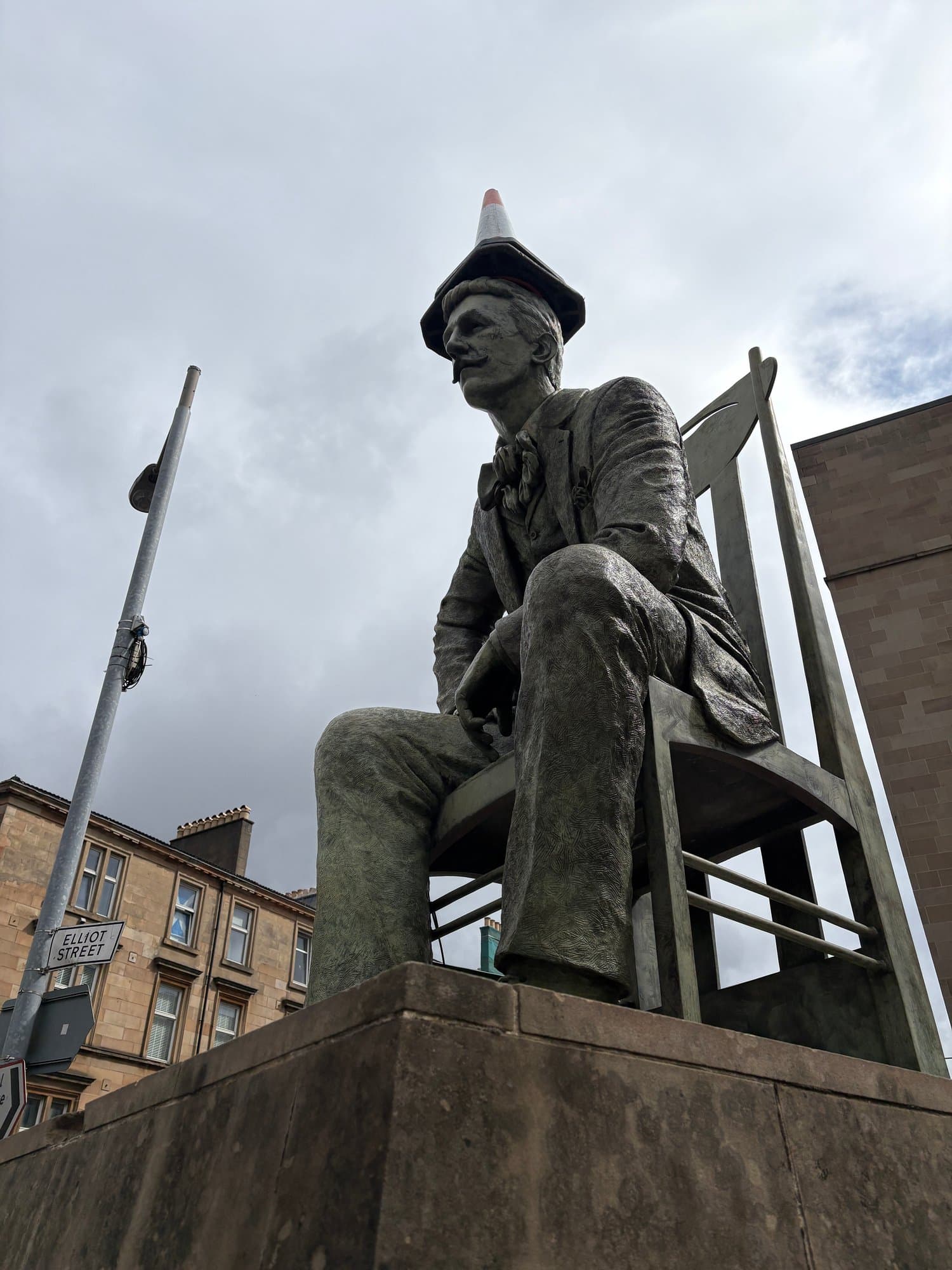 Bronze statue of Charles Rennie Mackintosh seated beside a tall chair