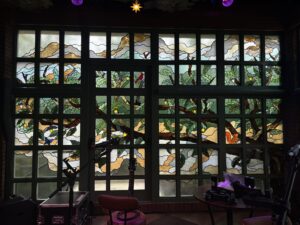 Large gridded window with tree branches and leaves in coloured glass