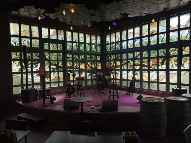 Corner of gridded windows filled with a coloured glass tree and birds, with a stage in front