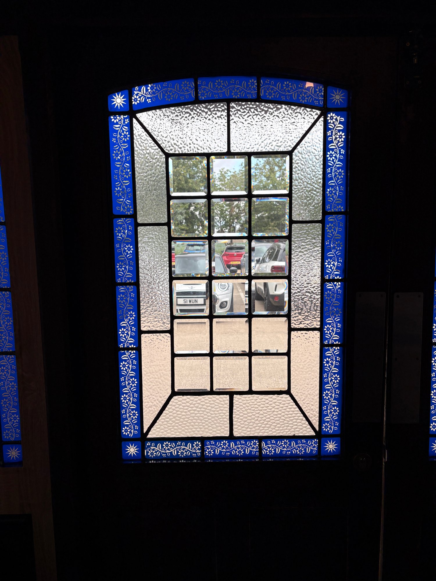 Door window with a blue border of white flowers and clear bevelled and textured glass, seen from outside
