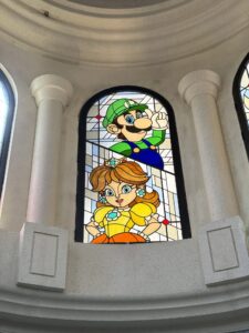 Arched window with two characters in a green cap and a yellow dress in leaded stained glass