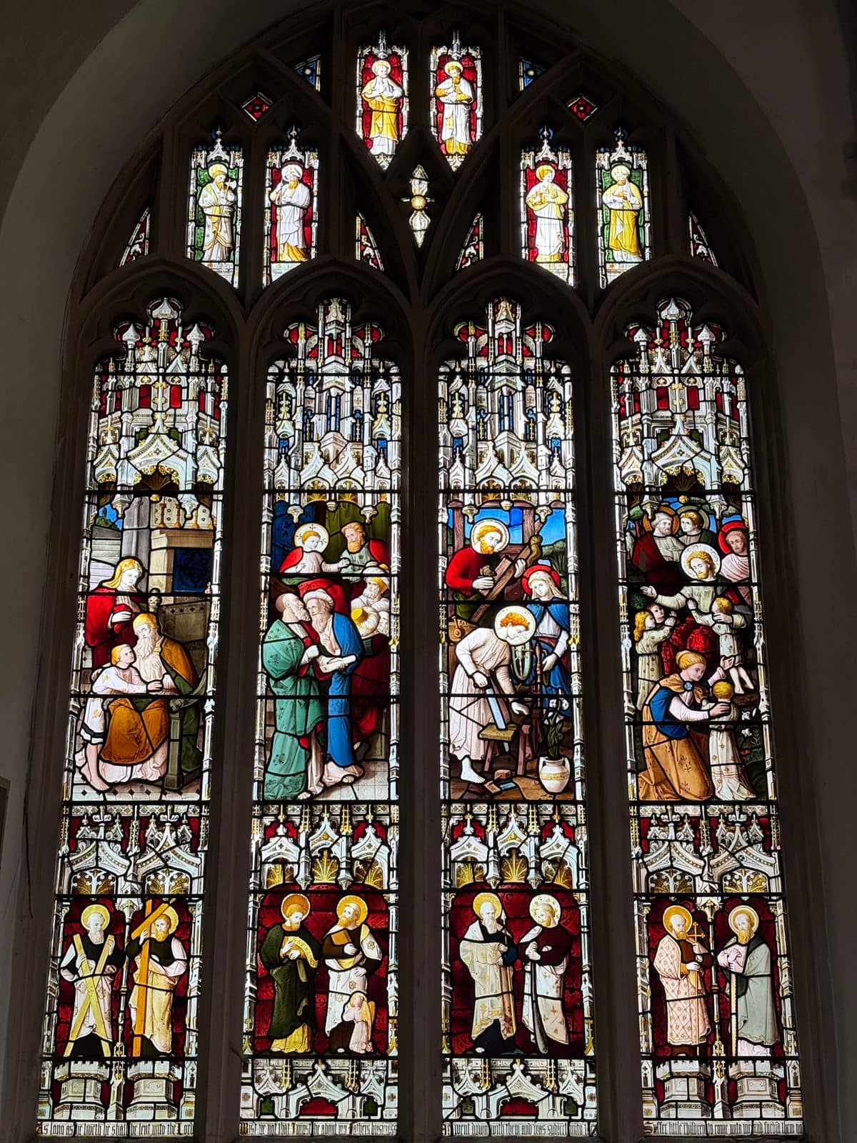 Tall Gothic church window with rows of coloured figures and scenes in stained glass