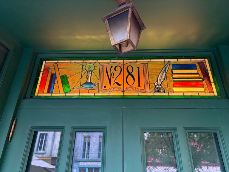 Stained glass transom above a green door showing a book, candle, quill and the number 281 on amber glass