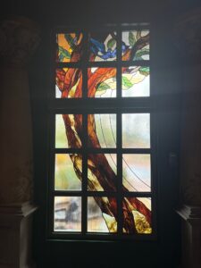 Tall window in grid panes with a tree trunk, leaves and blue birds in coloured and clear glass