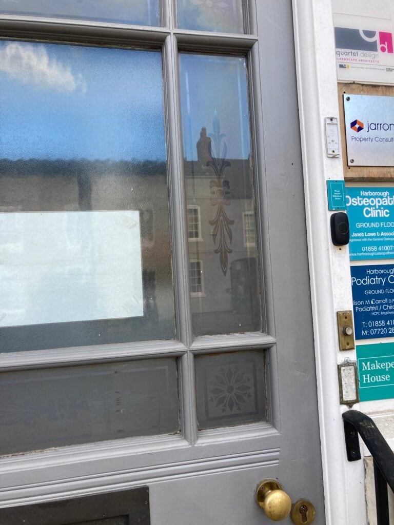 Grey painted door with etched glass panels showing a fleur-de-lis and a small rosette