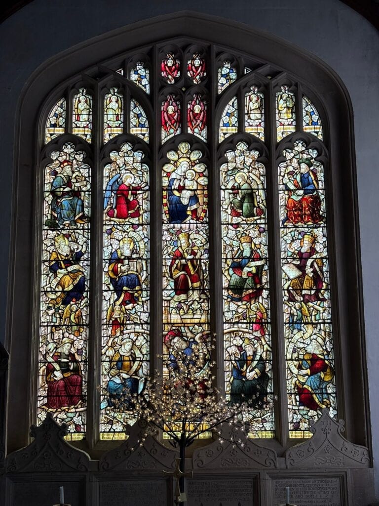 Five-light church window with seated figures and a lit candelabrum in front, Chippenham