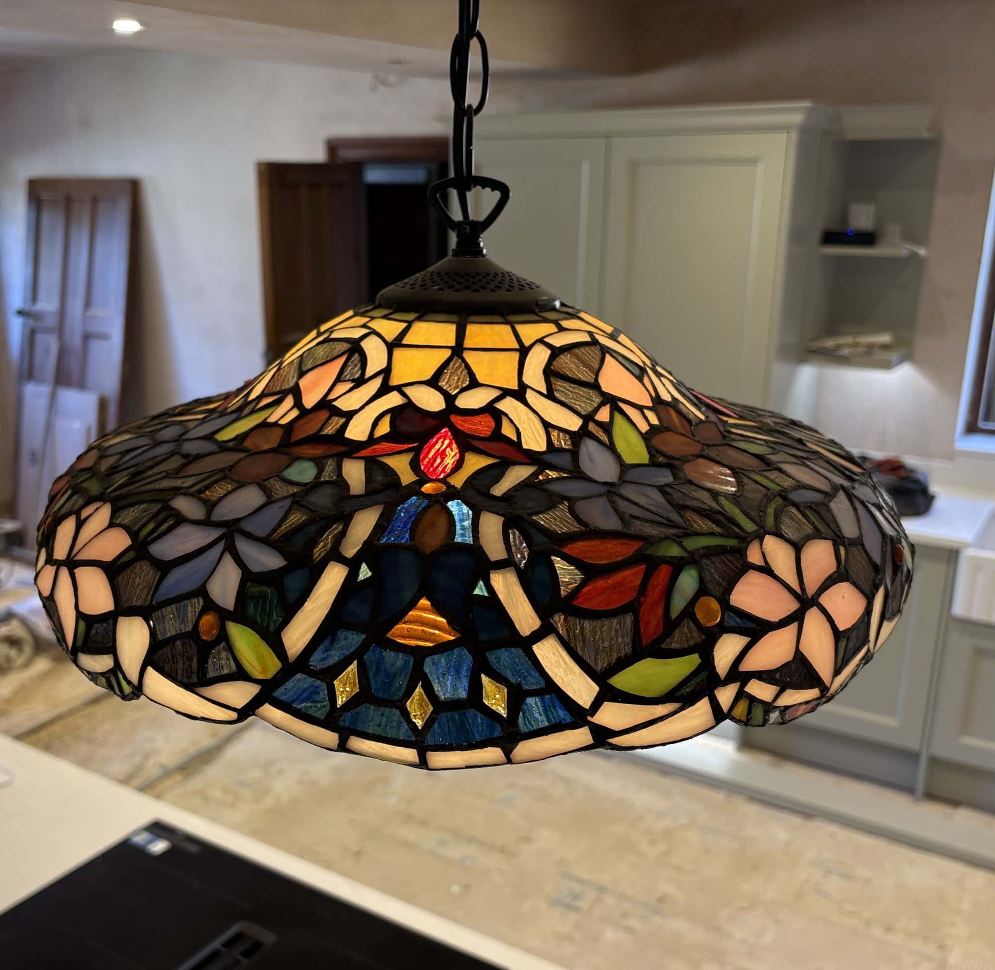 Close-up of a floral stained glass pendant lamp shade with pink flowers and a blue and amber border