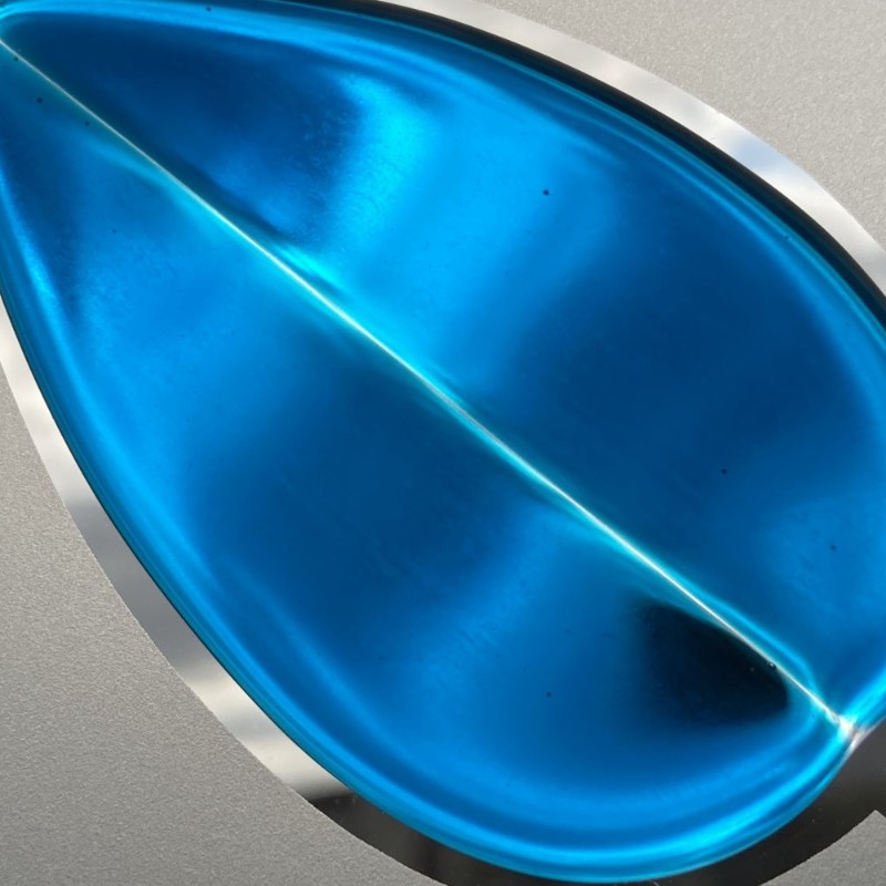 Close-up of a blue fused glass leaf set in a frosted glass panel with mirrored scrolling lines