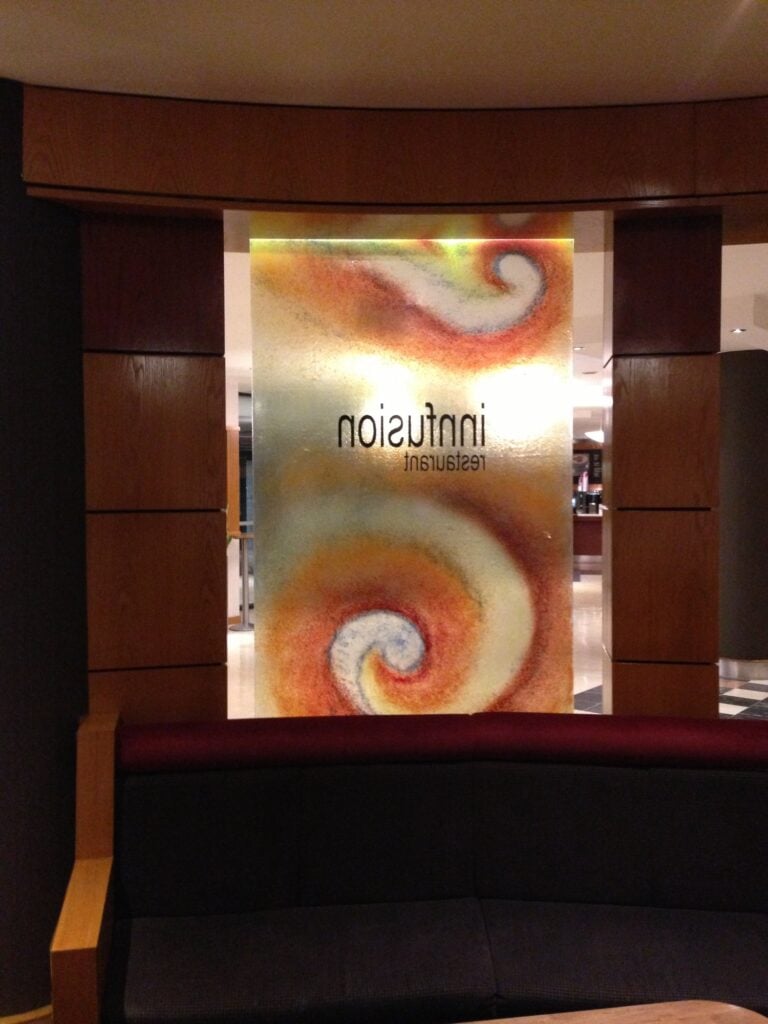 Back-lit fused glass panel with orange and cream swirls and mirrored restaurant lettering