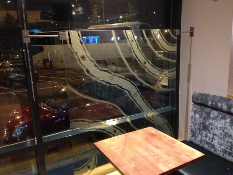 Night view of a glass screen with flowing ribbon lines and round glass jewels beside a restaurant table