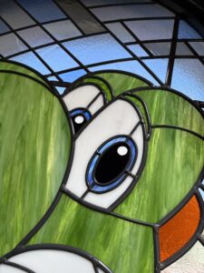 Close-up of a green dinosaur eye in stained glass with blue and white glass