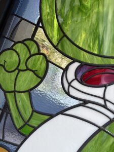 Close-up of a green dinosaur raised hand in stained glass with white and black leadwork
