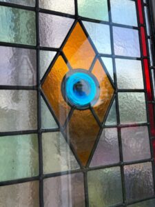 Pair of pointed leaded light windows with red borders, textured quarries and green, blue and amber roundels - another view