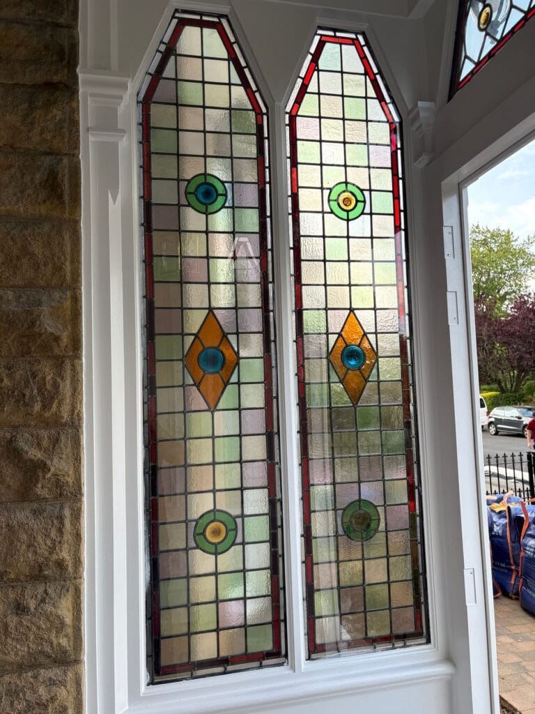 Pair of pointed leaded light windows with red borders, textured quarries and green, blue and amber roundels