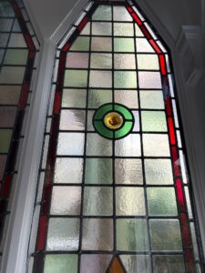 Pair of pointed leaded light windows with red borders, textured quarries and green, blue and amber roundels - second view