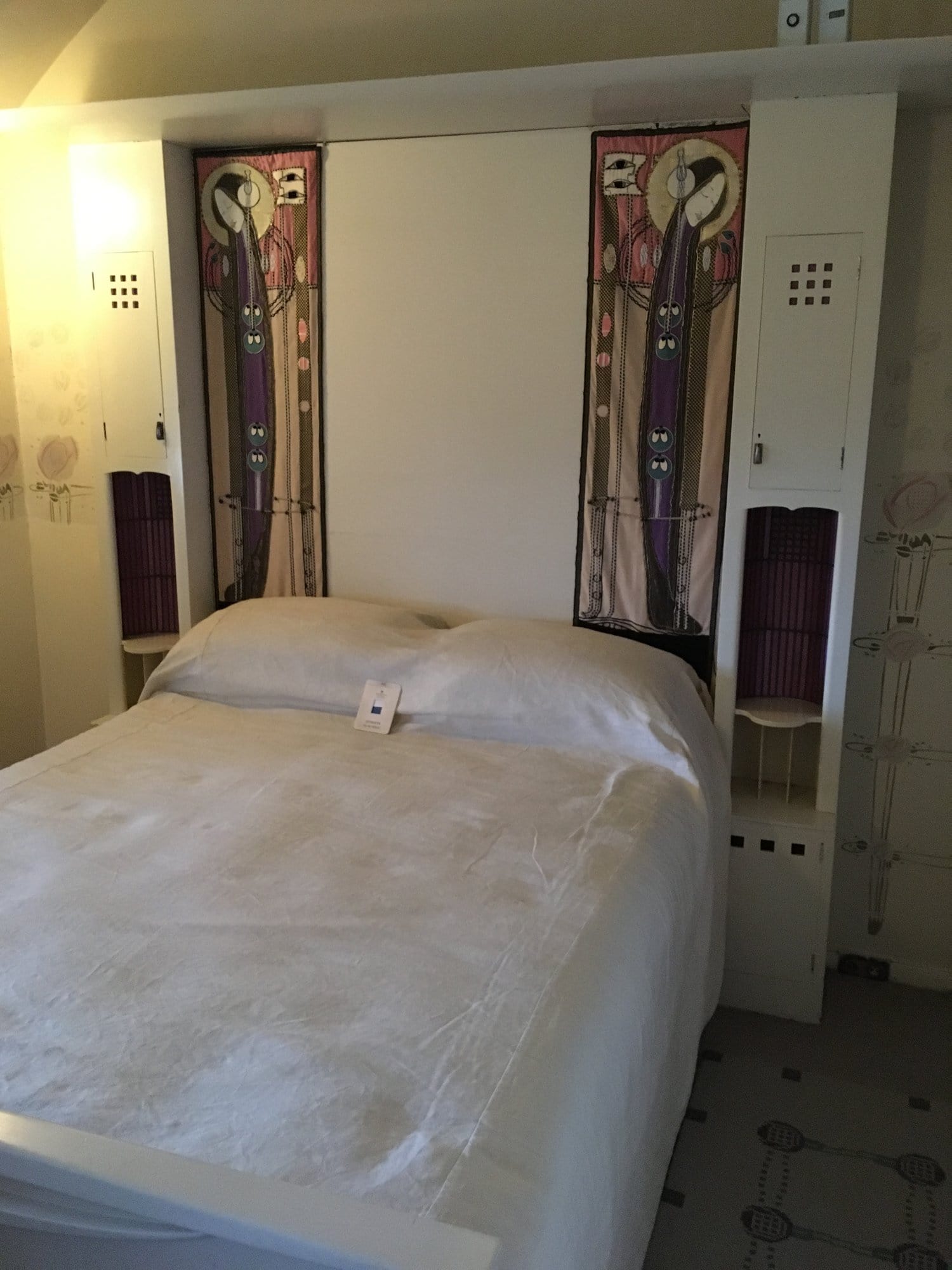 A white bed with tall decorated panels either side of the bedhead