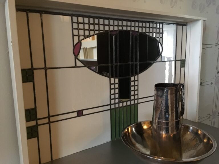 Washstand with a leaded glass panel and oval mirror in a bedroom at Hill House