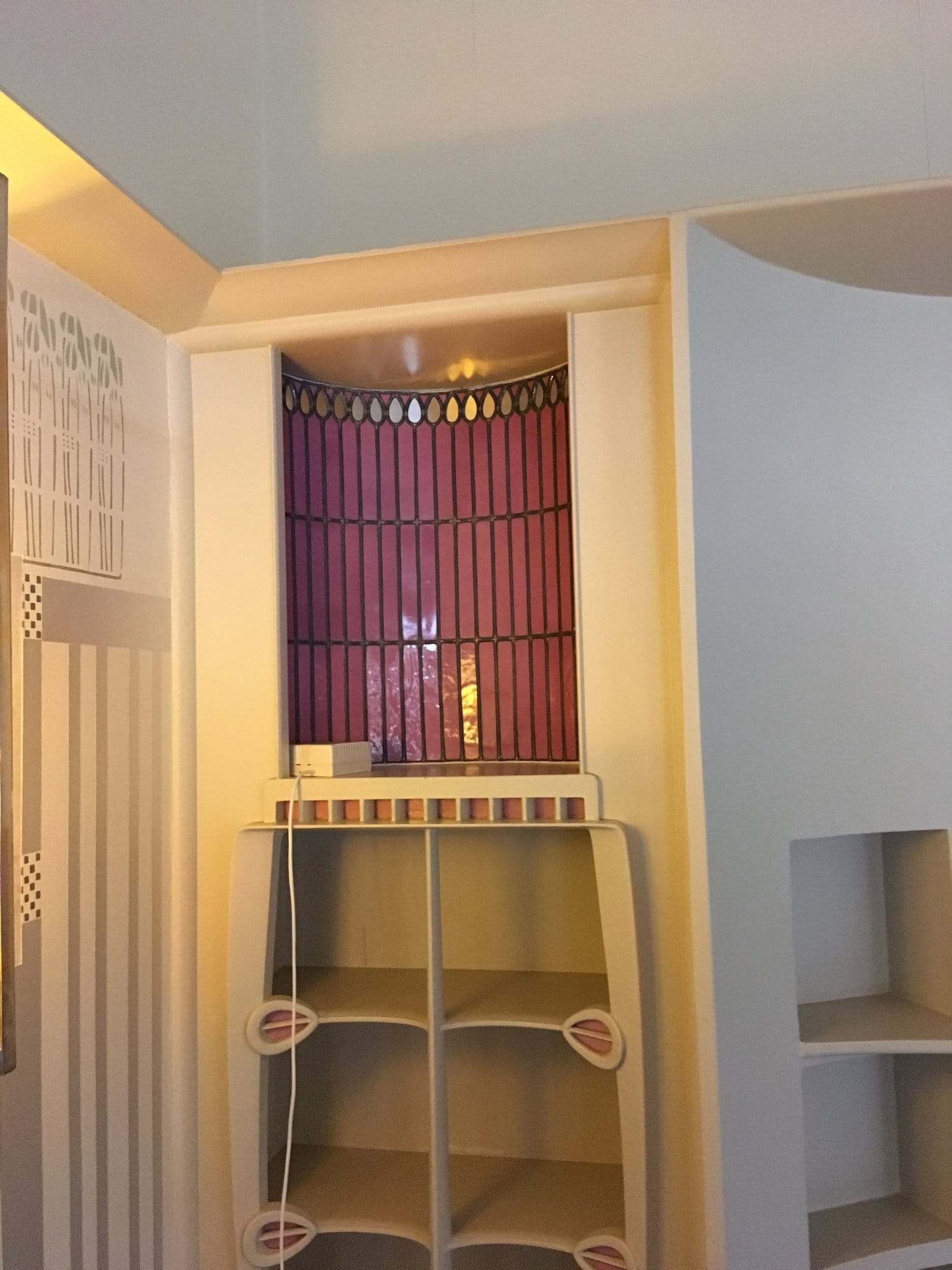 A curved niche with pink glass behind a small white shelf unit