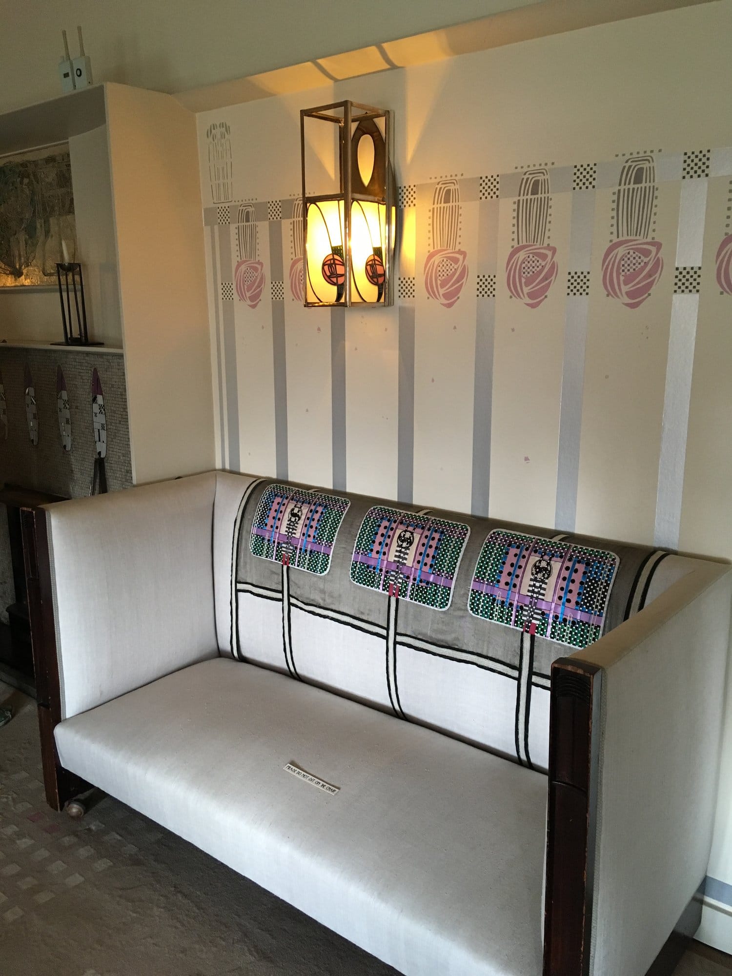 A white settle with a patterned back under a wall light and a rose frieze