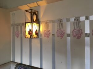 Wall lantern with rose motifs beside a stencilled rose frieze at Hill House