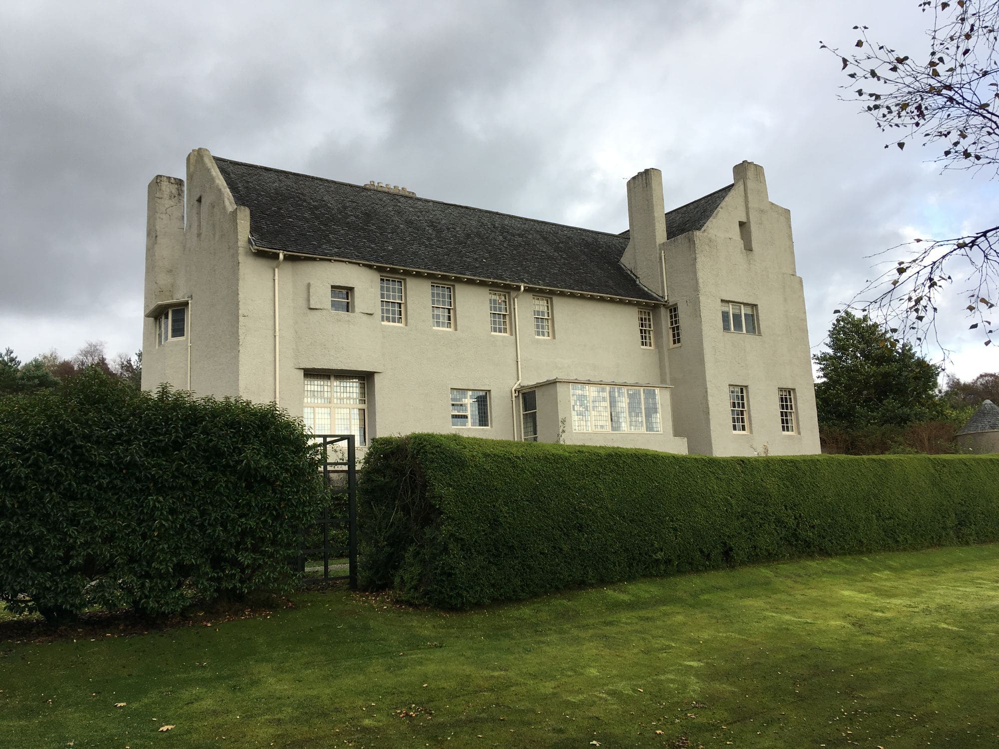 The side of Hill House behind a clipped hedge, with tall chimneys