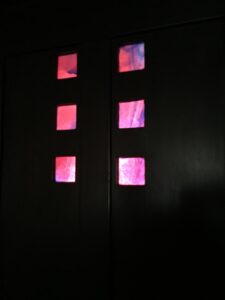 Small squares of red and pink glass set into dark panelling at Hill House