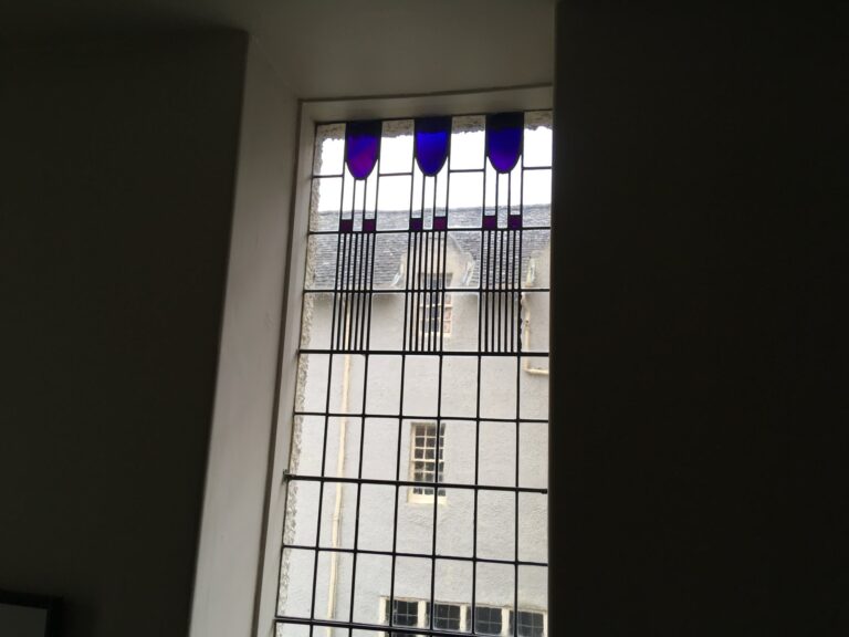 Tall staircase window with purple tulip shapes at the top in a lead grid at Hill House