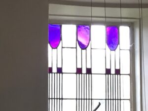 Window with a row of purple glass tulip shapes above a lead grid at Hill House