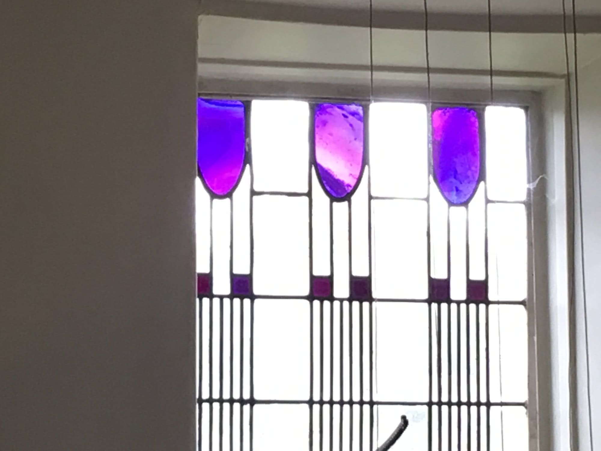 Window with a row of purple glass tulip shapes above a lead grid at Hill House