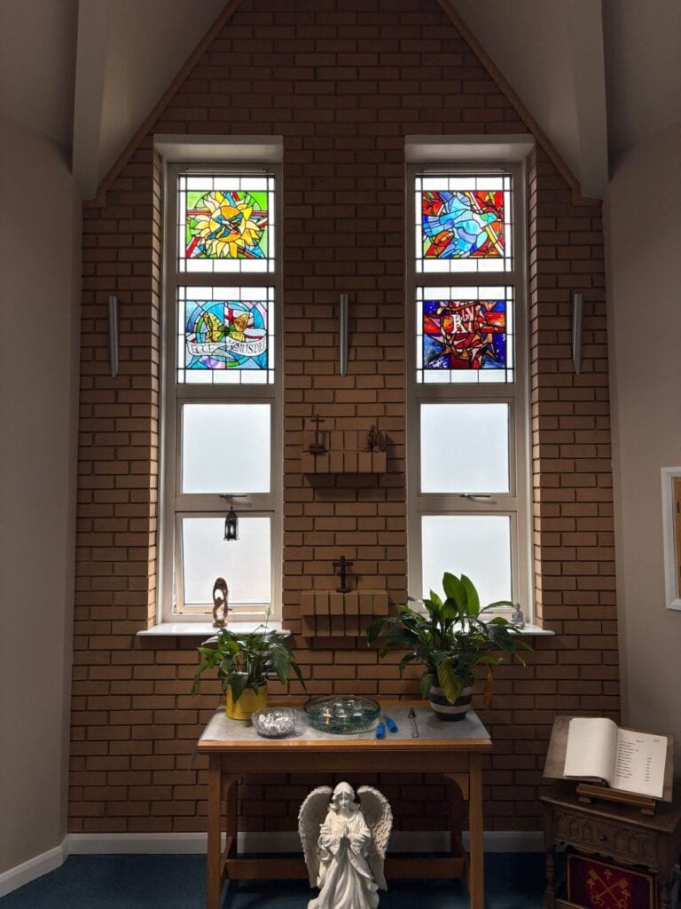 Chapel with two tall windows holding small stained glass panels above a table and an angel statue, Northampton