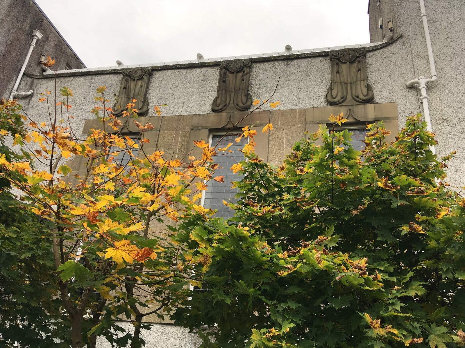 Carved stone panels high on the front wall of House for an Art Lover, behind autumn leaves