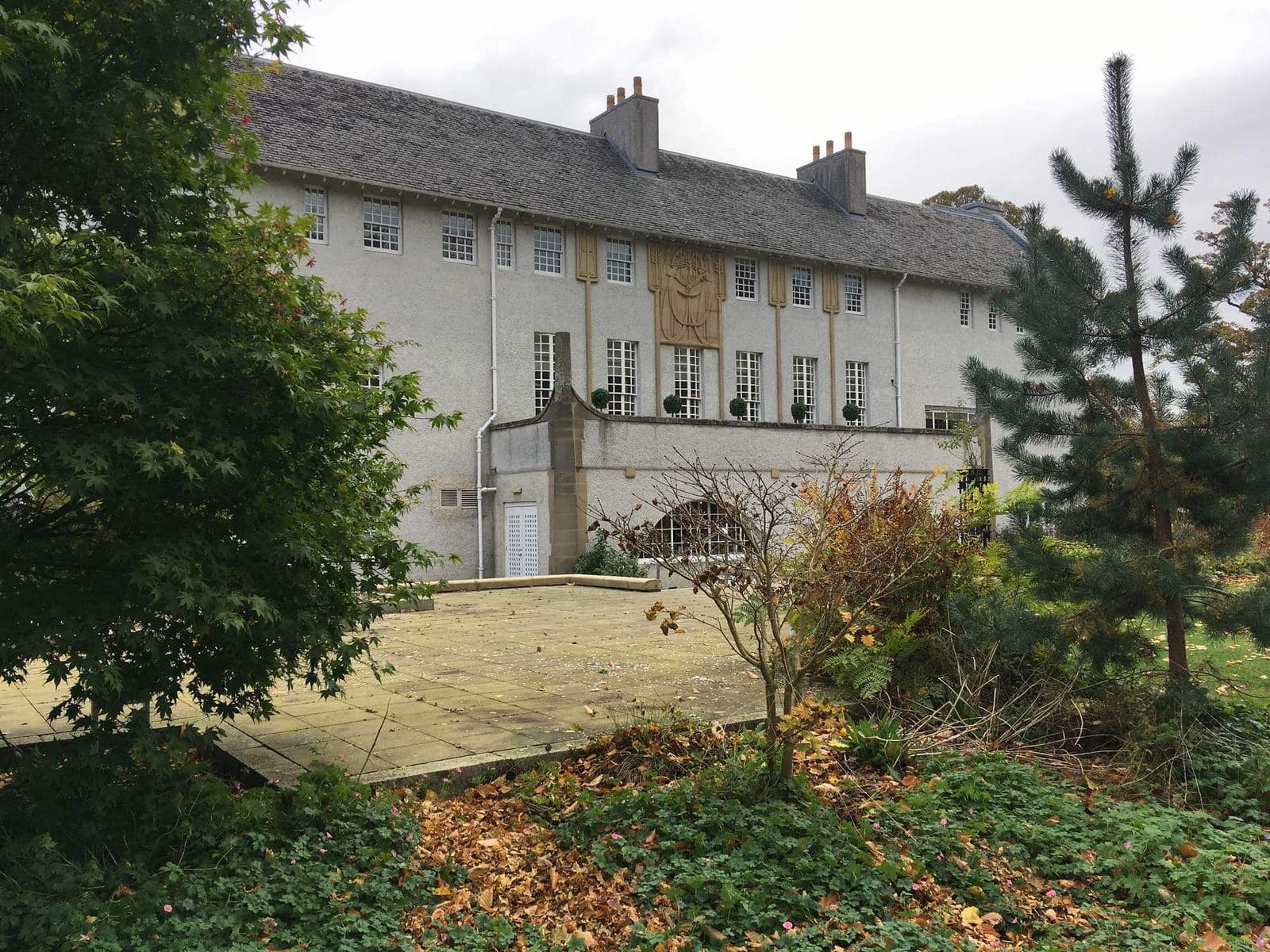 The long front of House for an Art Lover seen from the garden, with pine trees on the right