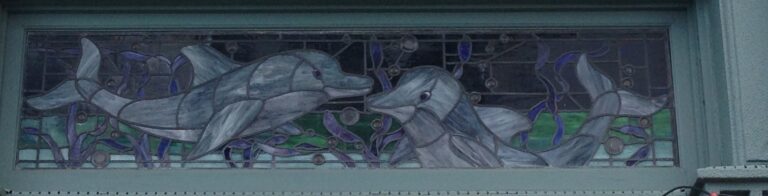 A long, narrow transom of leaded glass with a group of dolphins and sea plants in clear and pale glass.