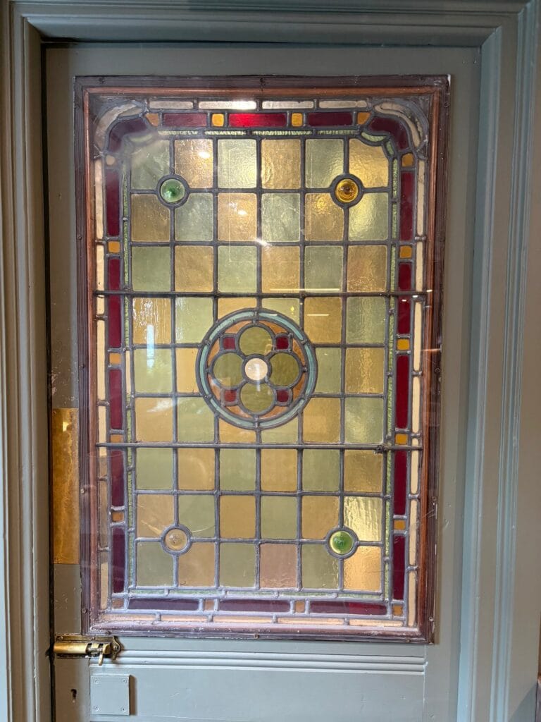 Leaded light door panel in pale amber and green squares with a central roundel and a red border