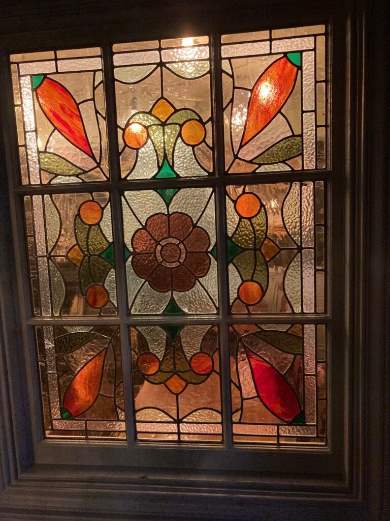 Leaded light window with a symmetrical flower design in orange, green and amber glass