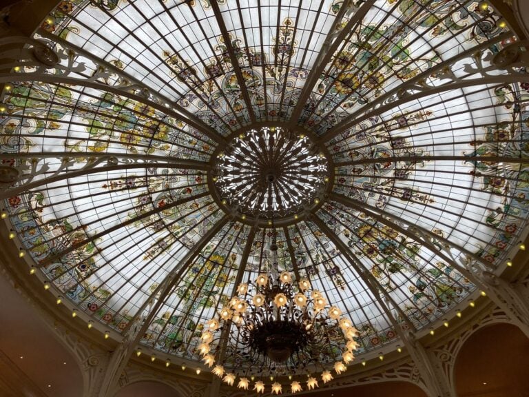 Circular domed glass ceiling of foliage panels with a central chandelier and ring of lights