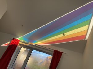 Rainbow light cast across a ceiling from a gable window