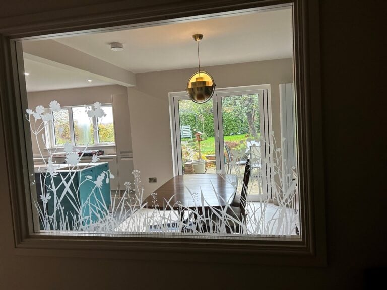 Internal window sandblasted with reeds and flowers, looking into a kitchen