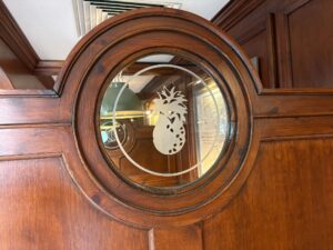 Pineapple roundel sandblasted into a round window in a wood panelled door