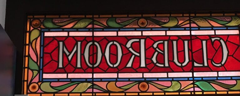 A red leaded panel with the words CLUB ROOM in pale glass and a border of scrolling leaves, seen from the back.