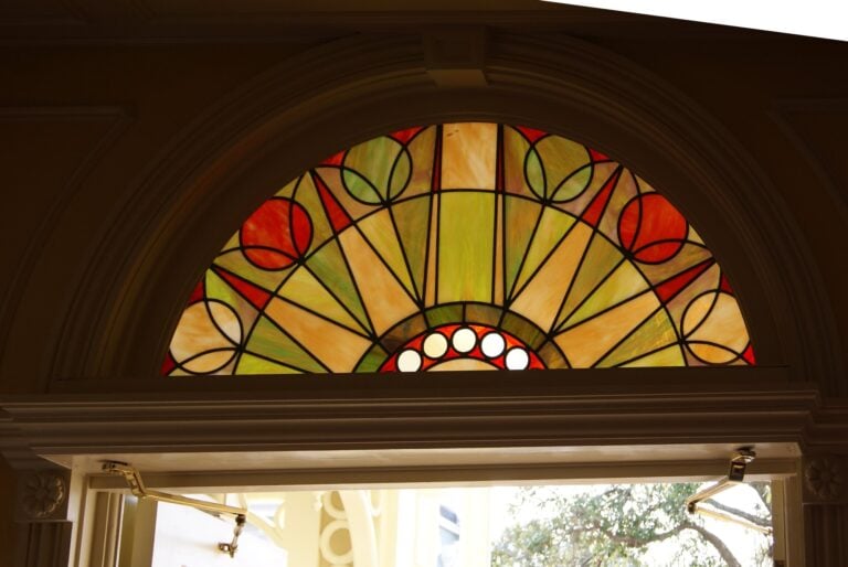 Semicircular fanlight of radiating amber and green segments with red circles above a doorway