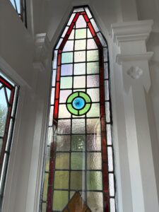 Tall pointed leaded window with red border and central roundel