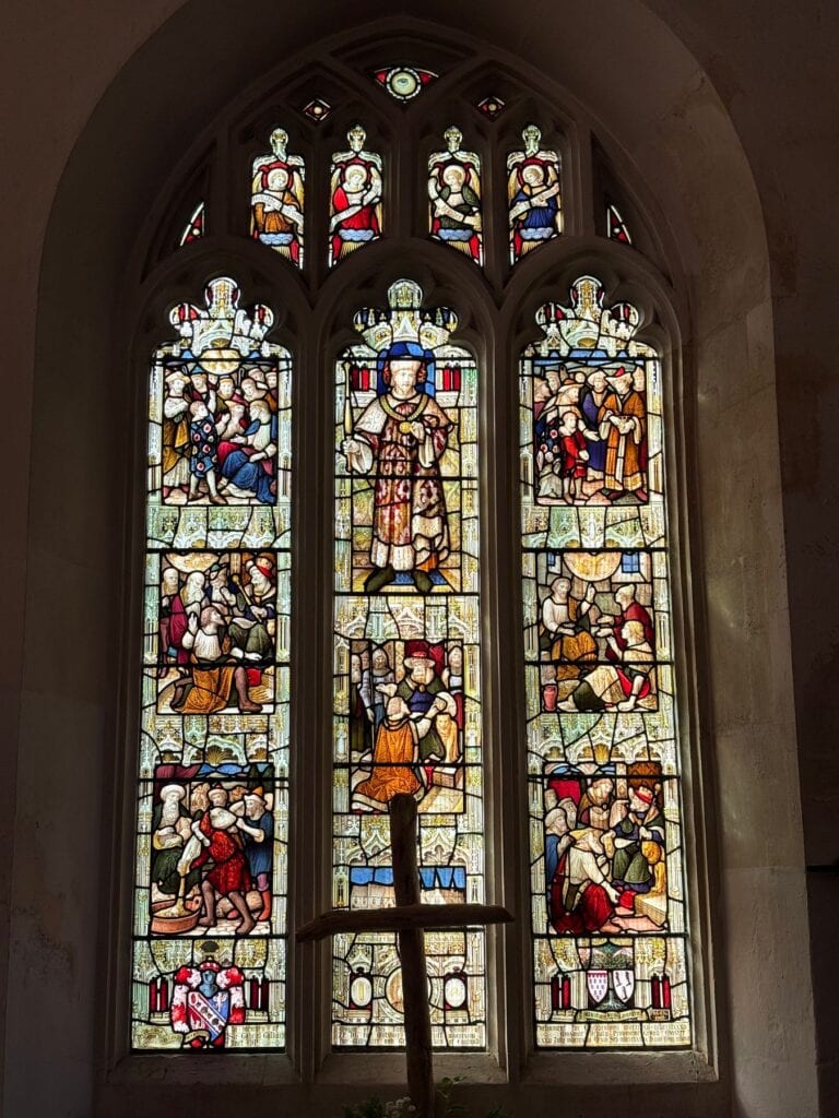 Three-light church window with a wooden cross in the foreground, Chippenham