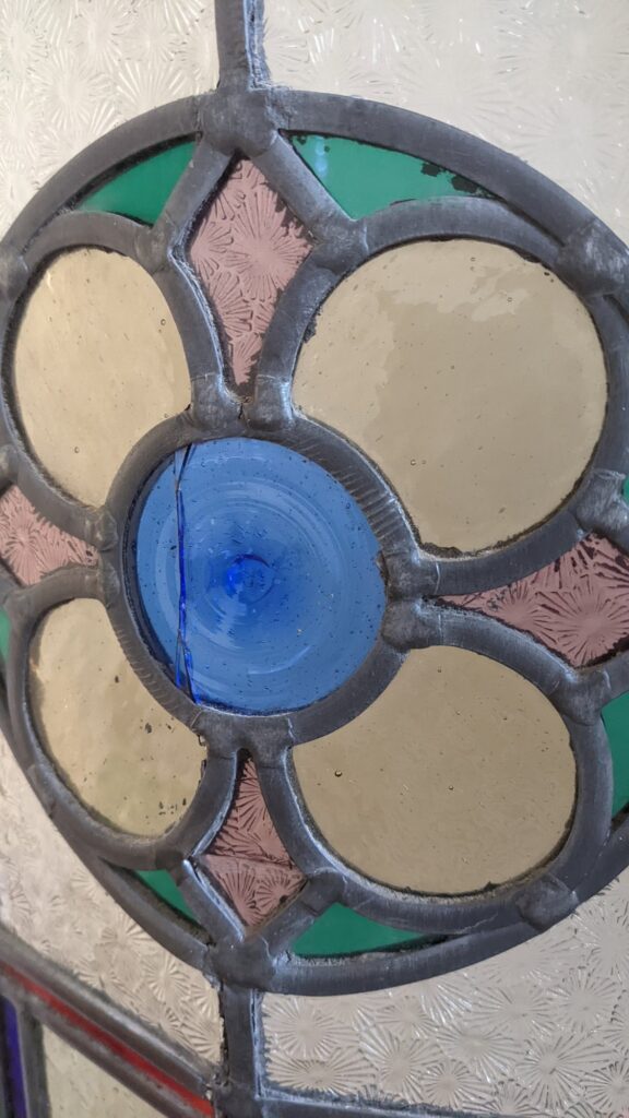 Close-up of a cracked blue roundel in a leaded door panel